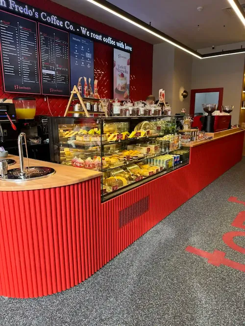 Kırmızı dikey oluklu panelli, doğal ahşap tablalı, entegre cam pasta ve sandviç vitrinli modern kurumsal cafe kasa bankosu