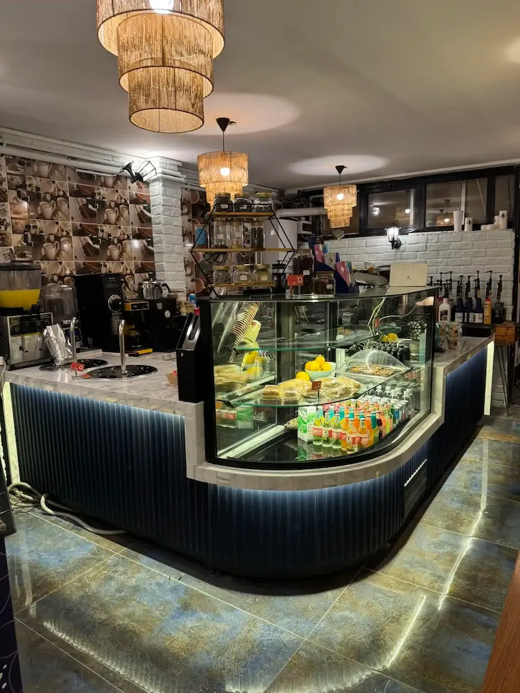 Gece mavisi dikey oluklu panelli, beyaz mermer tablalı, kavisli cam vitrinli ve alt LED aydınlatmalı lüks cafe teşhir bankosu