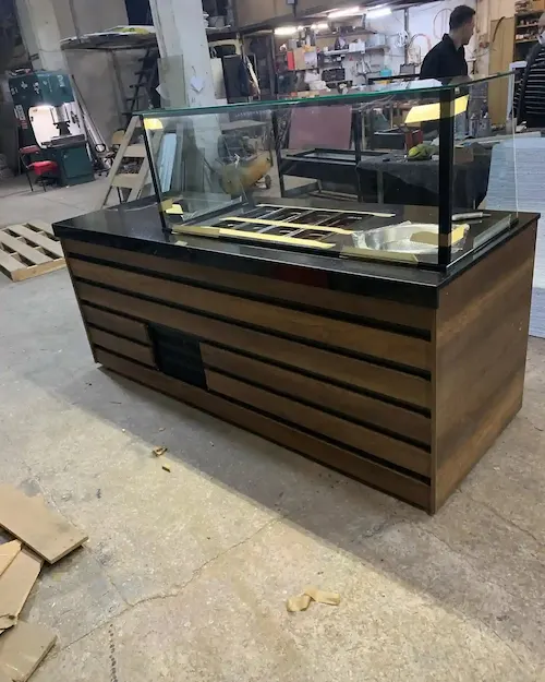 Koyu ahşap yatay panelli, siyah mermer tablalı, cam koruma vitrinli ve paslanmaz küvet hazneli modern çiğköfte tezgahı