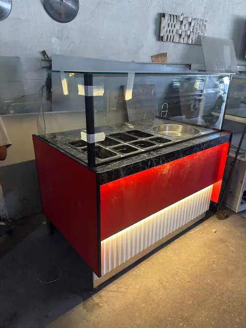 Kırmızı ön panelli, alt kısmı beyaz oluklu ve led aydınlatmalı, siyah mermer tablalı modern çiğköfte satış tezgahı