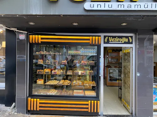 Siyah çerçeveli, yatay ahşap çıtalı, sarı led ışıklı dış mekan pastane vitrini ve soğutma dolabı