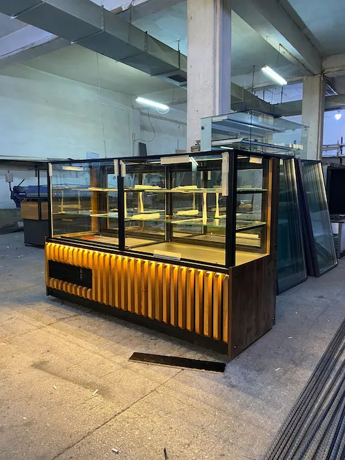 Ahşap çıtalı, sarı led aydınlatmalı, siyah metal profilli modern pasta ve tatlı teşhir dolabı