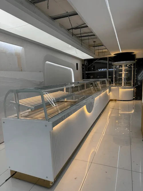 Beyaz lake oluklu panelli, gold baza detaylı, mermer tablalı ve led aydınlatmalı lüks modern pastane tezgahı projesi